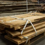 Dry unedged acacia boards stacked on a pallet with straps in a warehouse
