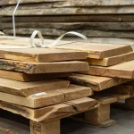 Joinery unedged acacia boards stacked on a wooden pallet in a warehouse.