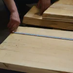 Measuring the length of an unedged acacia board with a tape measure