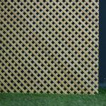 Oak lattice grille panel standing upright outdoors against a dark wall, with grass at its base.