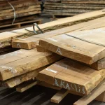 Width of kiln-dried live edge acacia boards stacked on pallets in a warehouse.