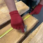 Worker in red gloves measuring the width of an unedged spruce board with a tape measure