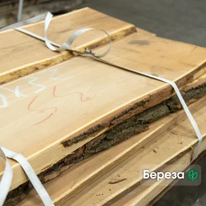 A strapped stack of unedged birch boards of Grade 1 showing natural bark edges and wood texture.