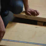 Measuring the width of a high-quality unedged birch board with a tape measure during quality control.