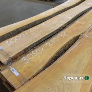 Unedged cherry wood boards of extra grade with handwritten dimensions in a warehouse.