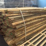 Strapped stack of unedged cherry lumber boards stored on a pallet in a warehouse.