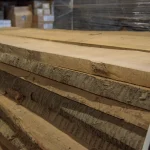 Side view of stacked unedged cherry boards showing natural bark on the edges.
