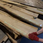 Inspection of a long unedged cherry board with chalk markings by a warehouse worker.