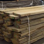 A neatly stacked pile of unedged red oak boards secured with straps in a warehouse.