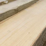 Texture close-up of a premium unedged red oak board showing the light wood grain and bark.