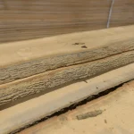 Close-up of the rough bark edges of stacked red oak boards, showcasing the natural waney-edge profile.