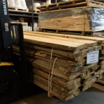 A forklift transporting a large bundle of Grade 1 unedged red oak boards with a product label in a warehouse.