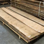 Stack of long unedged red oak boards on a wooden pallet in a warehouse.