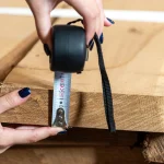 Measuring the thickness of a 52 mm Grade 1 unedged oak board using a tape measure.