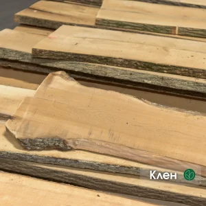 Stack of unedged maple boards of the first grade showing natural bark edges and light wood texture.