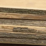 Side view of stacked unedged maple boards highlighting the thick natural bark layers on the edges.