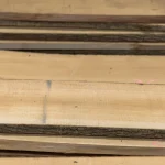 Close-up of the fine wood grain and natural bark edge of stacked unedged maple lumber.