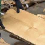 Worker in protective gloves holding a high-quality unedged maple board to demonstrate its clean surface.
