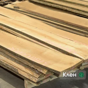 A stack of premium unedged maple boards with natural bark edges and chalk markings in a warehouse.