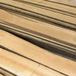 Top-down view of stacked unedged maple lumber showcasing natural waney edges and light wood tone.