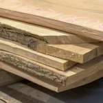Stacked ends of unedged maple boards with pink chalk markings indicating dimensions.