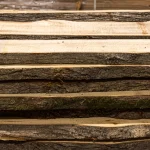 Side view of stacked unedged linden boards showing the textured bark on the edges.