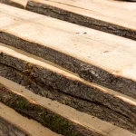 Close-up of stacked unedged linden boards showcasing their natural bark and wood layers.