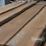 A stack of 1st grade unedged spruce boards showing natural bark edges and chalk markings.
