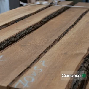 A stack of 1st grade unedged spruce boards showing natural bark edges and chalk markings.