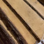 Top-down view of unedged alder boards showing natural wood grain and bark texture.