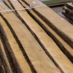 Stacked unedged alder boards secured with plastic strapping in a warehouse.