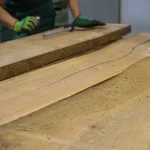 Woodworker inspecting and measuring an unedged alder board during quality control.