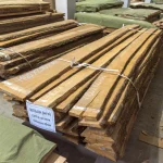 Stack of unedged alder boards (Extra grade, 32mm) in a warehouse with a specification tag.