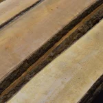 Diagonal view of several unedged alder boards highlighting their smooth surface and bark edges.