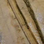 Close-up of unedged ash boards with chalk dimensions marked on the wood surface.