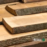 Close-up of unedged ash boards with natural bark edge stacked in a warehouse.