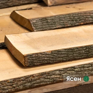 Close-up of unedged ash boards with natural bark edge stacked in a warehouse.