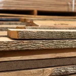 Side view of stacked unedged ash boards highlighting the bark texture and thickness.