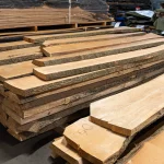 Multiple stacks of unedged ash boards of extra grade in a spacious lumber warehouse.
