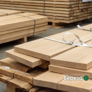 Close-up of stacked 1st grade edged birch boards secured with a white strap in a warehouse.