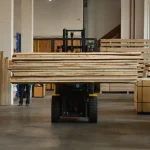 A forklift transporting a large stack of edged birch boards inside a spacious warehouse.