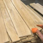 A worker in orange gloves selecting edged beech boards, 52 mm, in a warehouse.