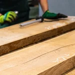 A worker inspecting and measuring dry edged cherry boards in a warehouse.
