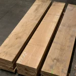 Three neat stacks of red oak edged lumber boards on a warehouse floor.