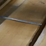 Measuring the width of an edged red oak board with a metal tape measure.