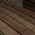 Wood grain texture of 52 mm American black walnut edged boards stacked in a warehouse.