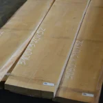 Edged maple boards marked with dimensions in a warehouse.