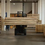 Forklift transporting a large stack of edged maple boards inside a spacious warehouse.