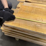 Measuring the width of an edged spruce board using a tape measure in the warehouse.