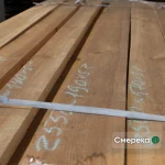 Close-up of stacked edged spruce boards with handwritten chalk dimensions and a white packing strap.